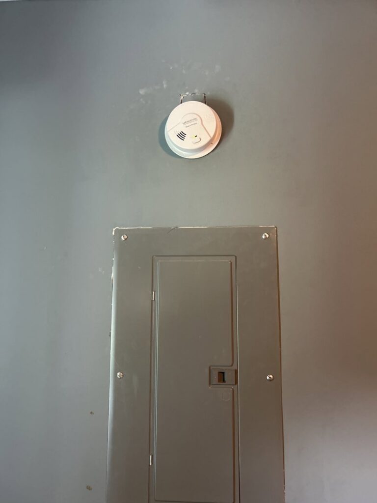 A smoke detector installed above an electrical panel by Mister Sparky Kansas City, MO.