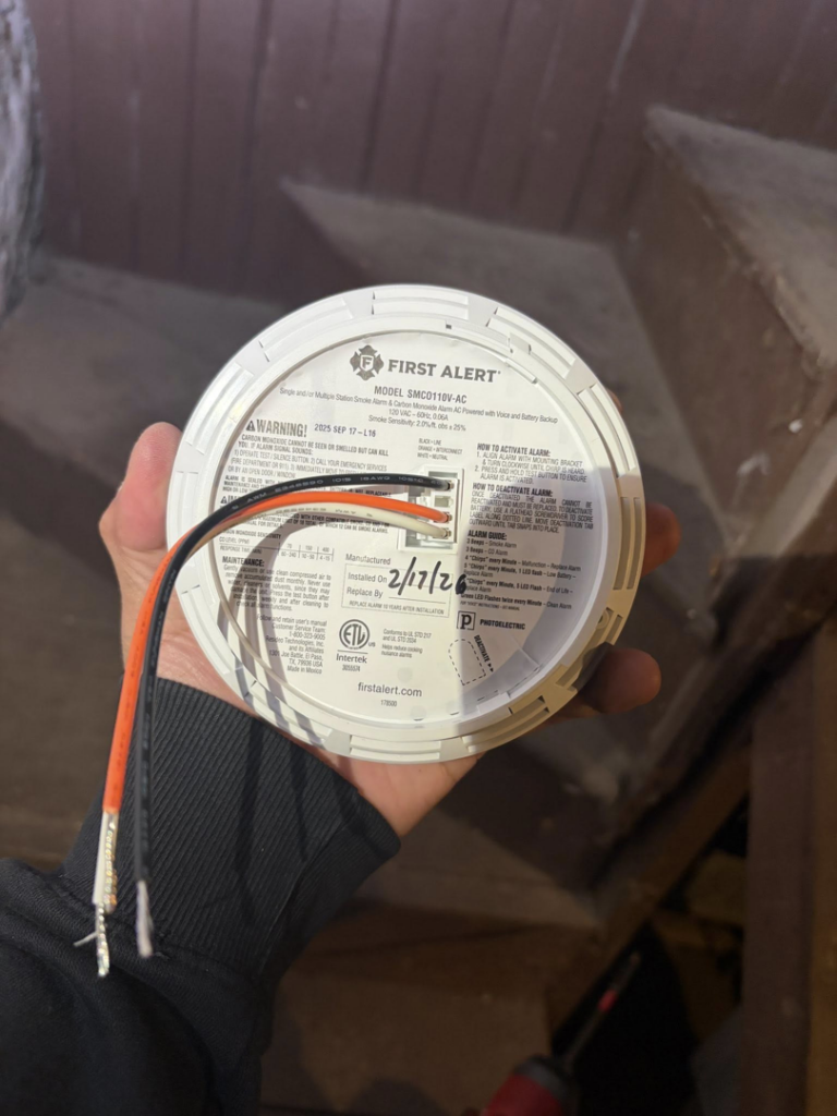 An electrician holding a smoke detector showing its wiring connections for installation by Dartmouth Fire Protection Electrical Division in New Bedford, MA.