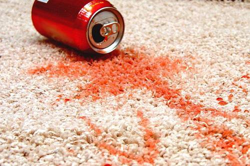 A red soda can spilled on a light-colored carpet, indicating a stain that ABC Chem-Dry St. Louis in St Charles, MO can remove.