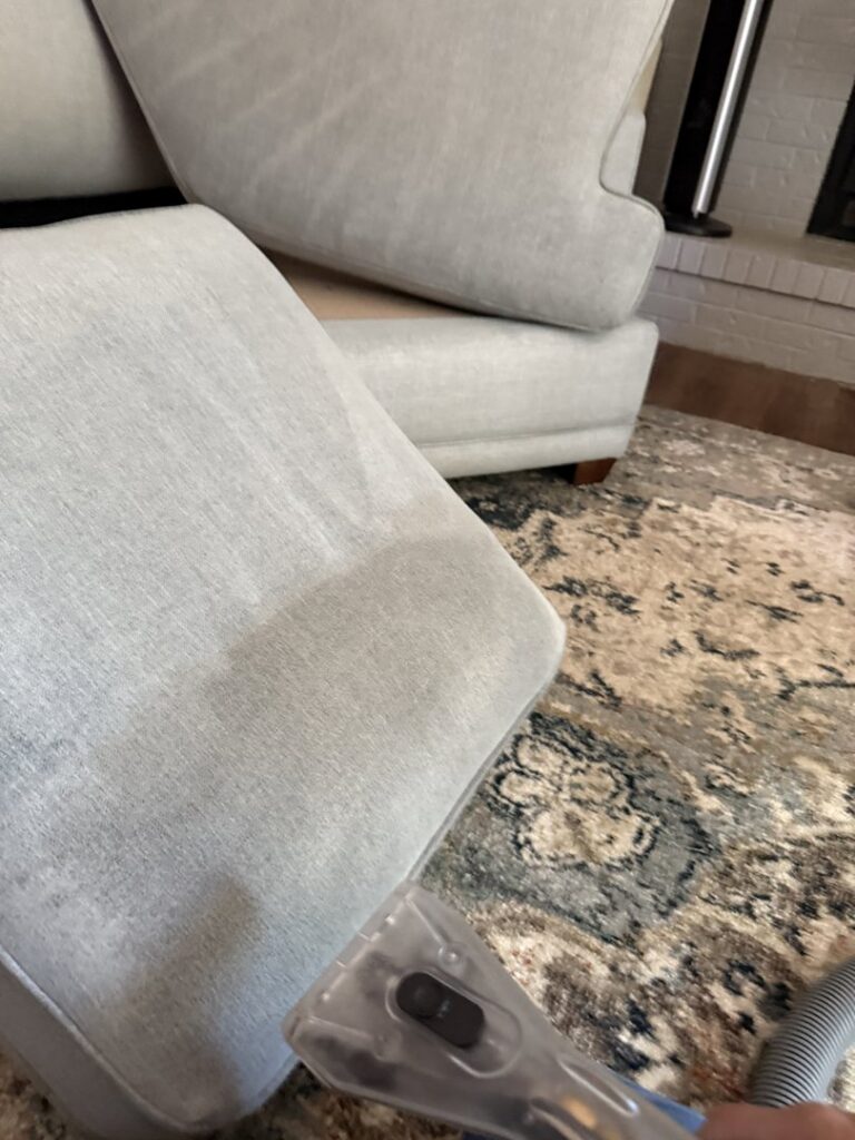A professional cleaning a sofa cushion with an upholstery tool at Believe That Carpets & Upholstery Cleaning in Colorado Springs, CO.