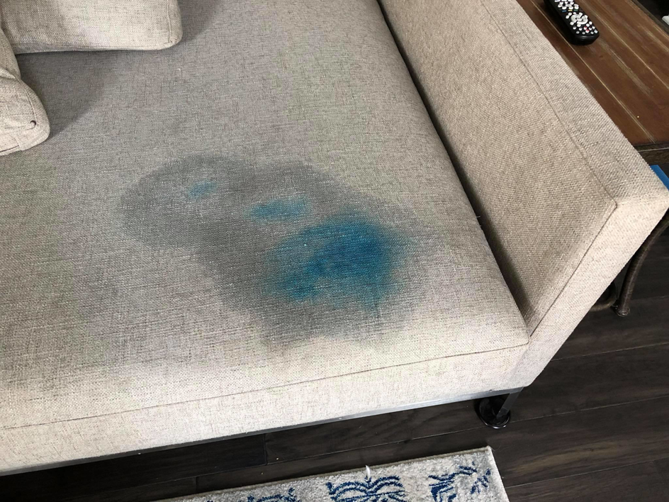 A light-colored sofa with a prominent blue stain on the cushion before cleaning by Erich's Carpet Care in Blue Springs, MO