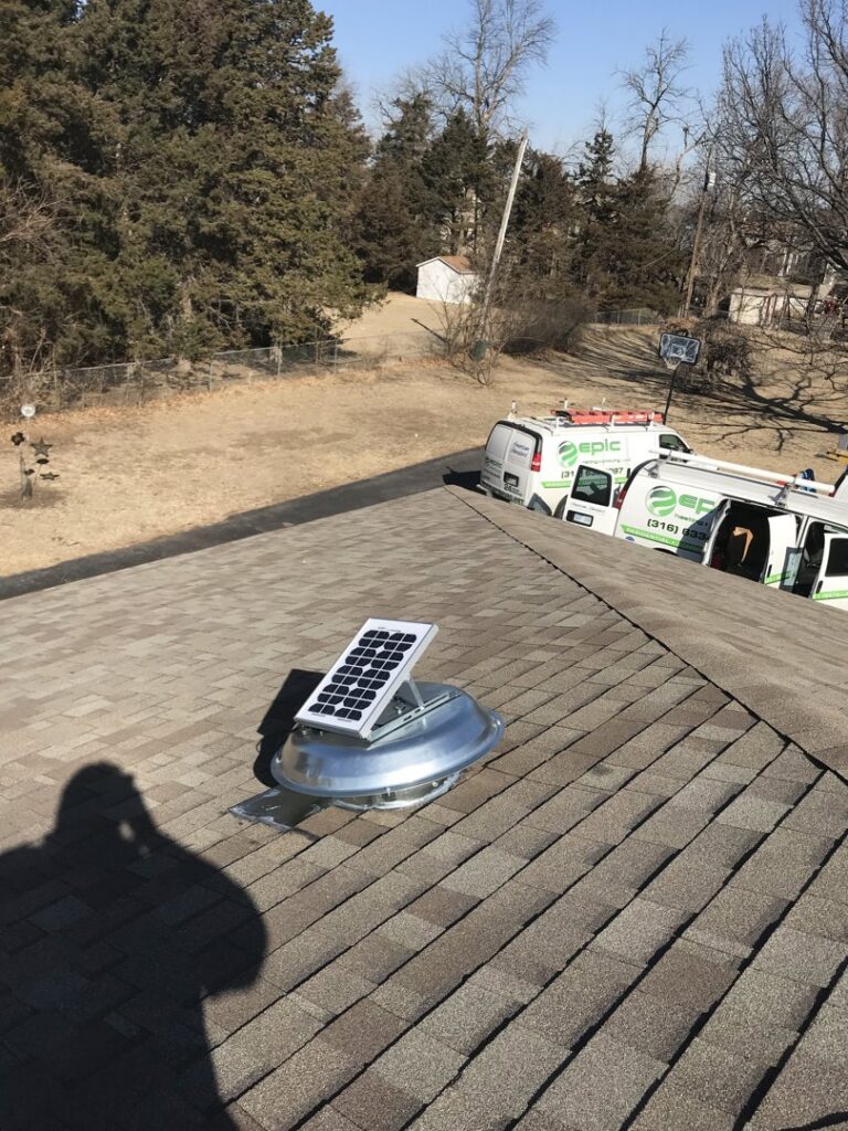 A solar-powered attic fan installed on a roof by Epic Heating & Cooling in Wichita, KS, with company vans in the background.