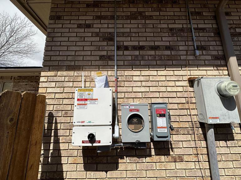 Exterior electrical panels and conduits for a solar system installed on a brick wall by Pueblo Electrics, Inc. in Pueblo, CO.