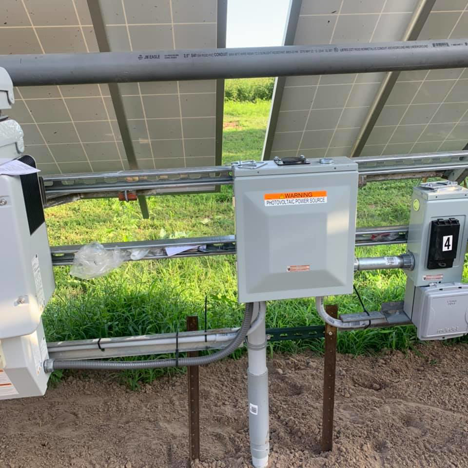 An electrical junction box with a "Photovoltaic Power Source" warning installed under solar panels by Affordable Electric, LLC in Kearney, NE.