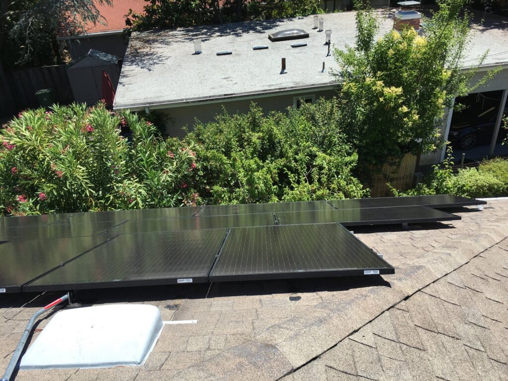 Solar panels installed on a shingle roof, surrounded by lush greenery by Solar & Electric Service Bros in West Sacramento, CA.