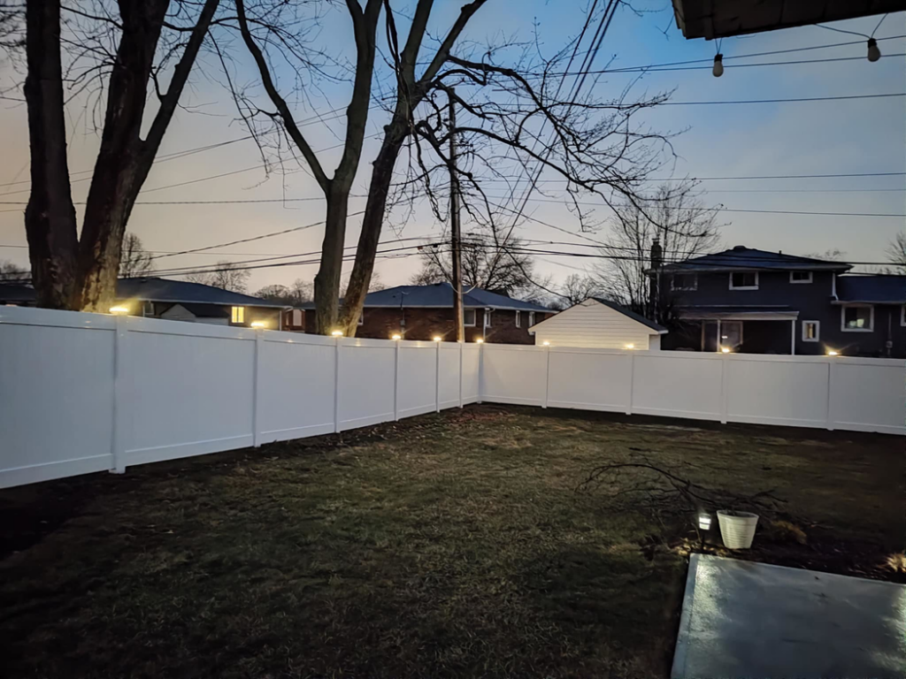 A spacious backyard enclosed by a white vinyl fence with decorative post lights, installed by Fence Guys INC in Cleveland, OH.