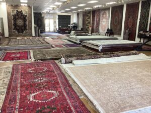 A spacious rug showroom displaying a wide variety of rugs on the floor at Woven Treasures, Inc in Mobile, AL.