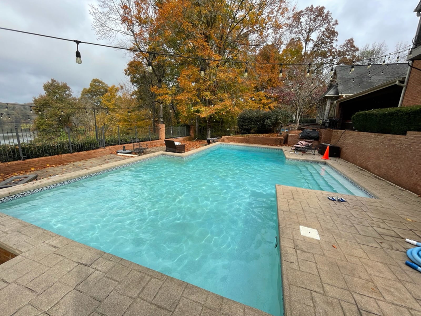 A sparkling clean swimming pool with a hose on the deck, maintained by Pristine Pools of Knoxville, TN.