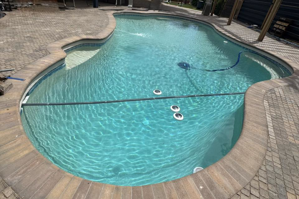 A sparkling blue swimming pool with a robotic pool cleaner in action, maintained by Brigade Pool Services in Tempe, AZ.