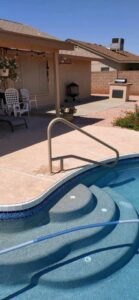 A sparkling clean pool with steps and a handrail, with a pool hose visible, indicating professional service from Space Ranger Pools in Gilbert, AZ.