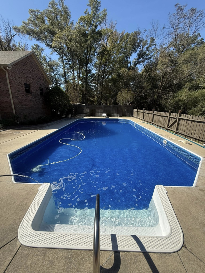 A sparkling clean swimming pool with a pool cleaner hose visible, maintained by KS Pool Co. LLC in Auburn, AL.