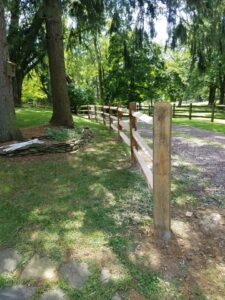 A split rail fence installed alongside a gravel driveway and mature trees by Concord Fence Llc in Wilmington, DE