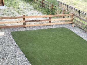 A wooden split-rail fence with wire mesh installed around an area with artificial turf and gravel by First Rate Fence & Supply in Denver, CO.