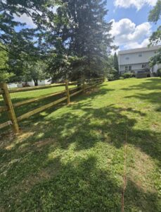 A split rail fence with added wire mesh for enhanced security in a grassy area by Concord Fence Llc in Wilmington, DE