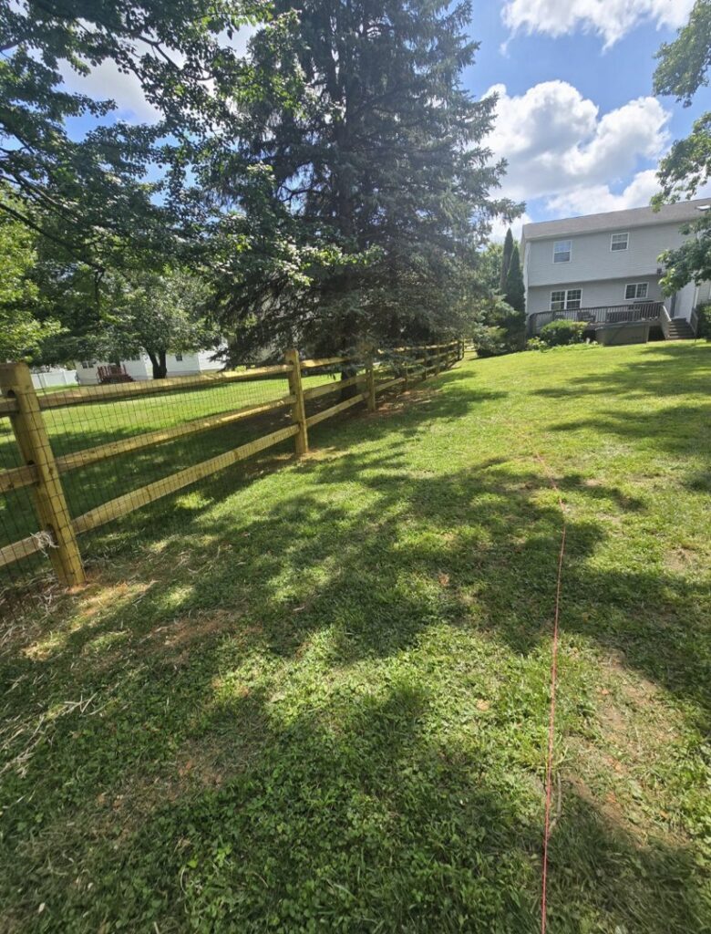 A split rail fence with added wire mesh for enhanced security in a grassy area by Concord Fence Llc in Wilmington, DE