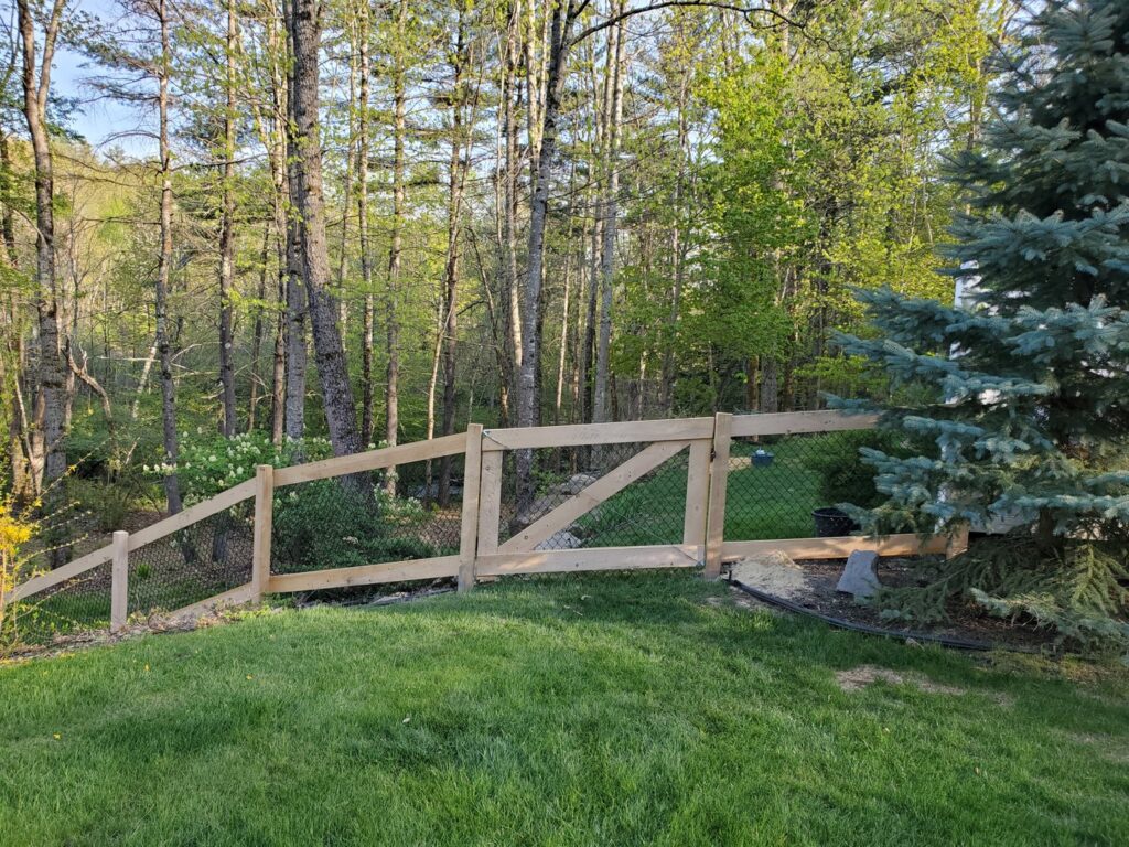 A rustic split rail fence with wire mesh installed in a residential yard by MH Fence in Weare, NH.