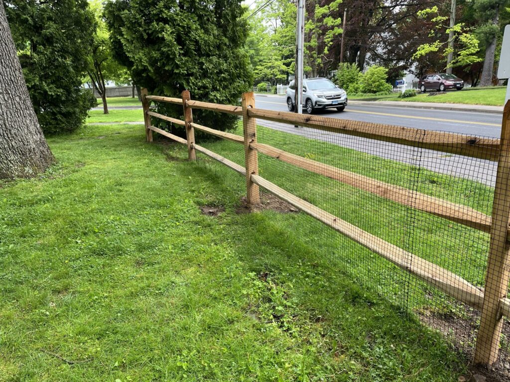 A rustic split rail fence with added wire mesh, installed along a roadside by AVA Fence & Railing LLC in Stamford, CT.