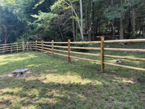 A split rail fence with wire mesh and a gate in a wooded area by Quality Fence Inc. in Peekskill, NY.