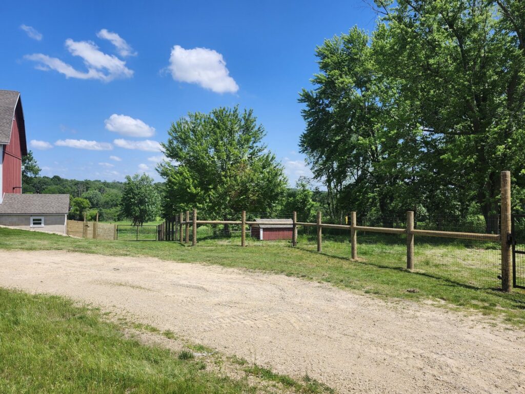 A completed split rail fence with wire mesh installed along a property line by H&S Fencing & Supply in Linden, WI.