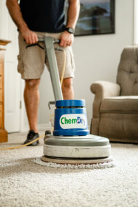 Chem-Dry Spot Remover bottle on a rug with a technician cleaning a spot in the background at H-Town Chem-Dry in Spring, TX