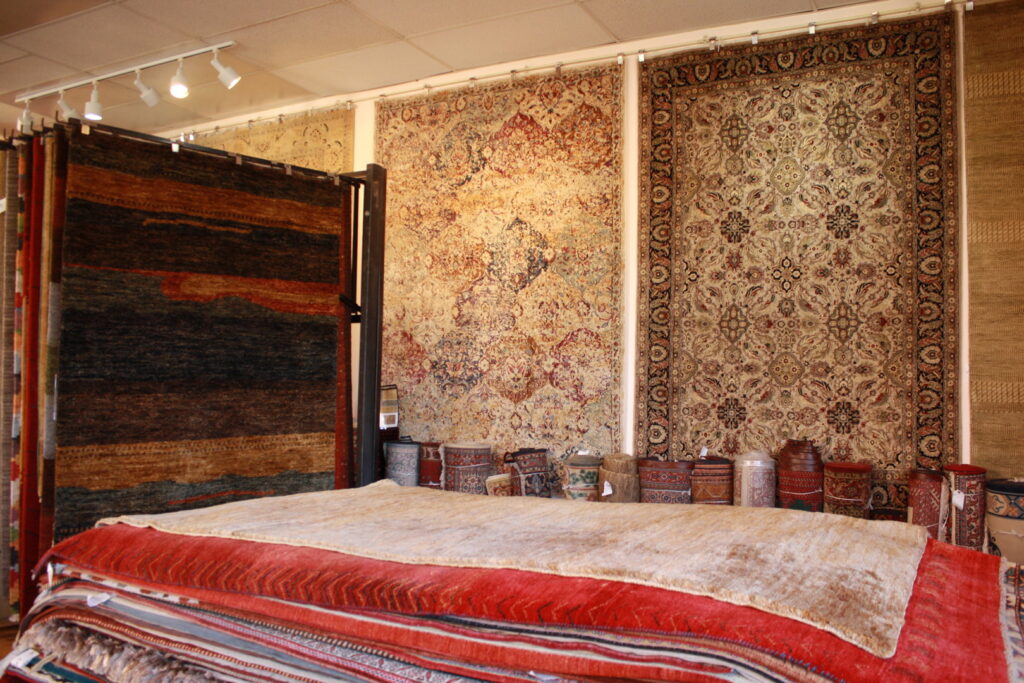 Various rugs stacked on display tables and hanging on walls in the showroom of Ebie's Rug Cache & Ebie's Rug Cleaning in Tucson, AZ