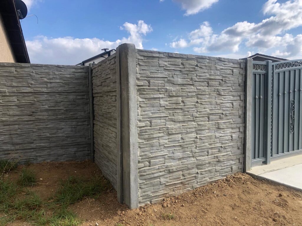A stacked stone texture concrete fence with a dark metal gate by StackWall Manufacturing in Pomona, CA.