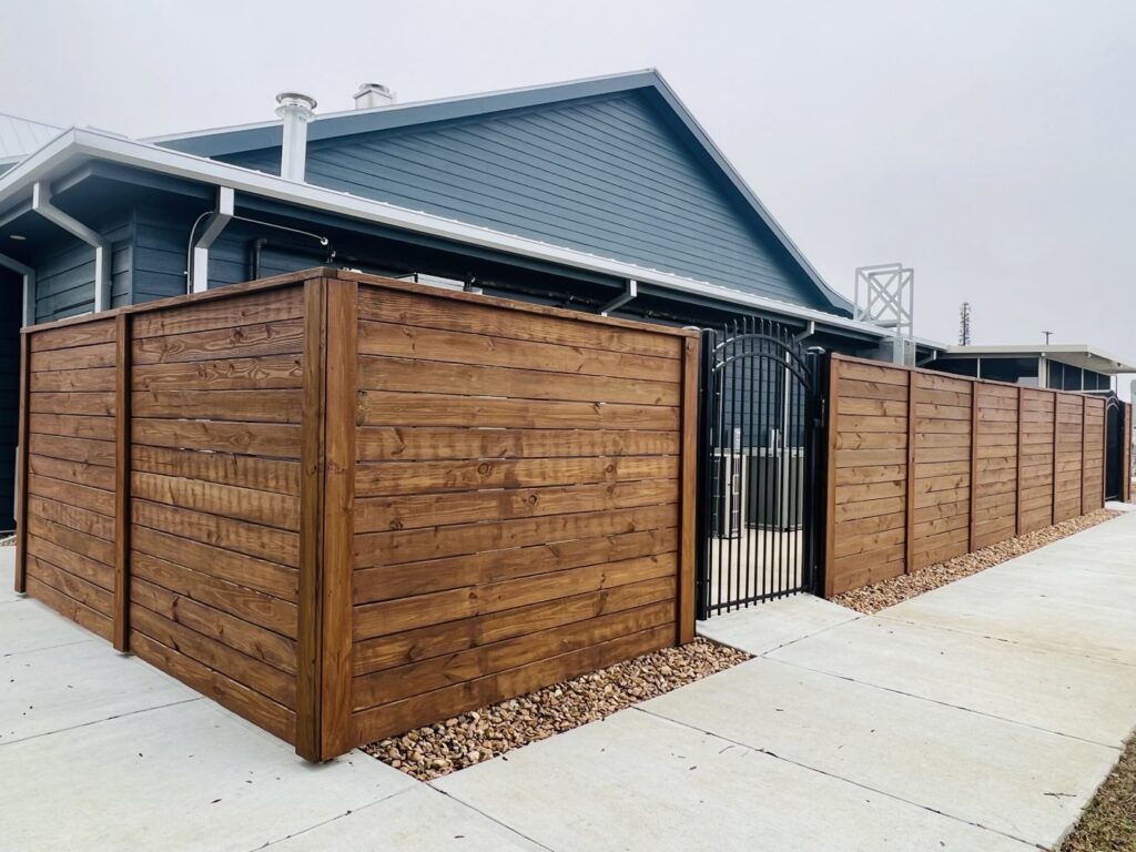 A stained horizontal wooden privacy fence with a decorative black metal gate, installed by Capitol Fencing in Baton Rouge, LA.