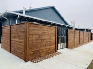 A stained horizontal wooden privacy fence with a decorative black metal gate, installed by Capitol Fencing in Baton Rouge, LA.
