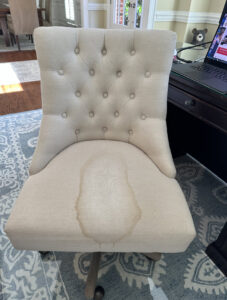 A light-colored upholstered chair with a noticeable stain, ready for cleaning by Steamworks Carpet and Upholstery Cleaners in Matthews, NC.