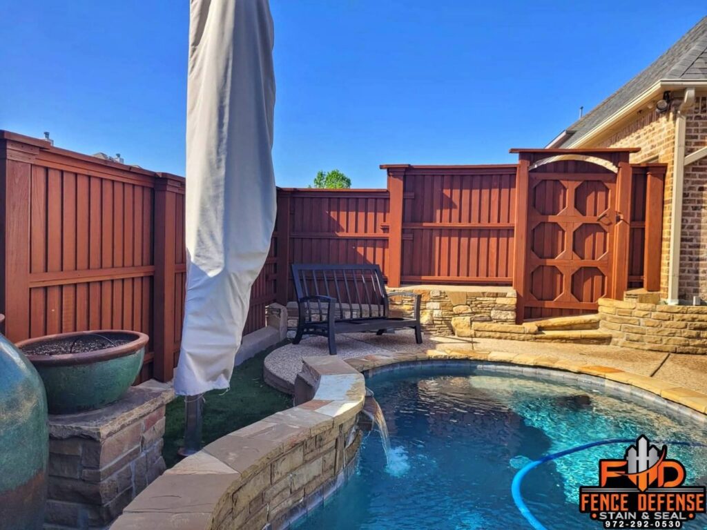 A stained wood fence with a custom gate and top trim next to a poolside area by Fence Defense in Plano, TX