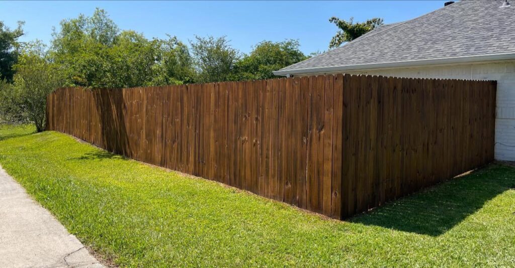 A beautifully stained wooden privacy fence lining a residential property, installed by JH Fencing in Lawrence, KS.