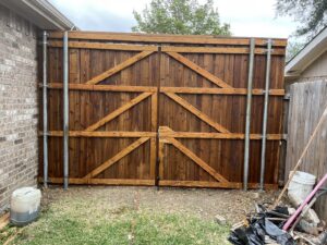 A newly installed stained wooden double gate with sturdy metal posts by G L Fence & Remodeling in Arlington, TX.