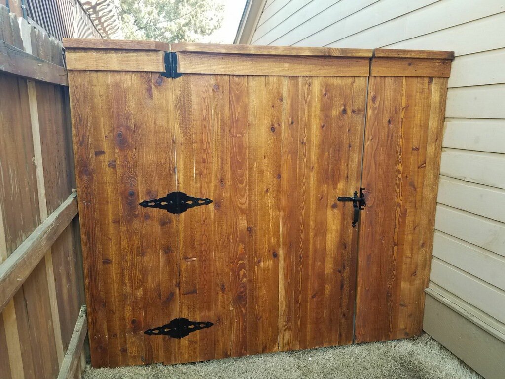 A stained wooden fence gate with black hardware installed next to a residential home by Frontline Fence Company in Fulton, NY