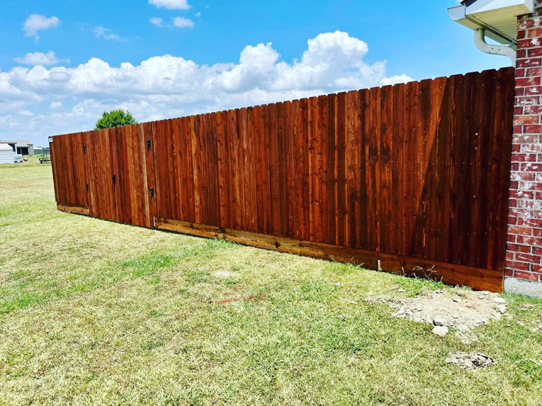 A newly installed stained wooden privacy fence next to a brick house, completed by HammerHorn Fence & Gate Systems in Rochelle, IL.