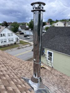 A newly installed stainless steel chimney liner and cap on a roof by Granite State Chimney in Manchester, NH