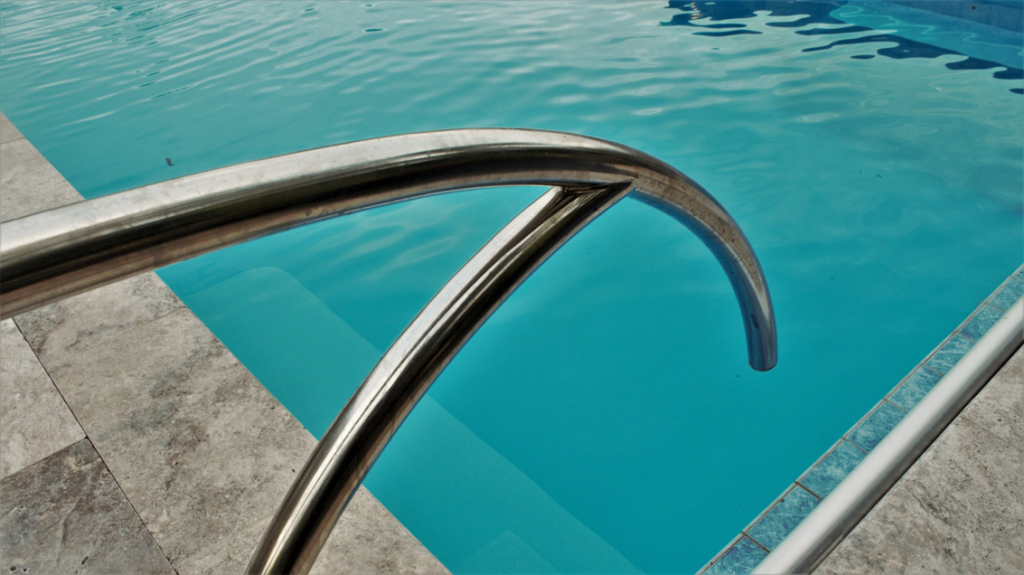 A stainless steel pool handrail with tiled edges, installed by Midwest Custom Pools, LLC in Lawrence, KS.