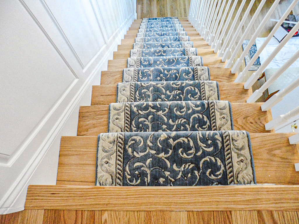 A beautifully installed blue and white patterned carpet runner on a wooden staircase by RugSale by Kaoud Rugs in West Hartford, CT.