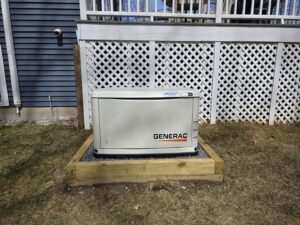 A standby generator professionally installed on a gravel bed next to a home's deck by Cason Power Solutions in Lowell, MA