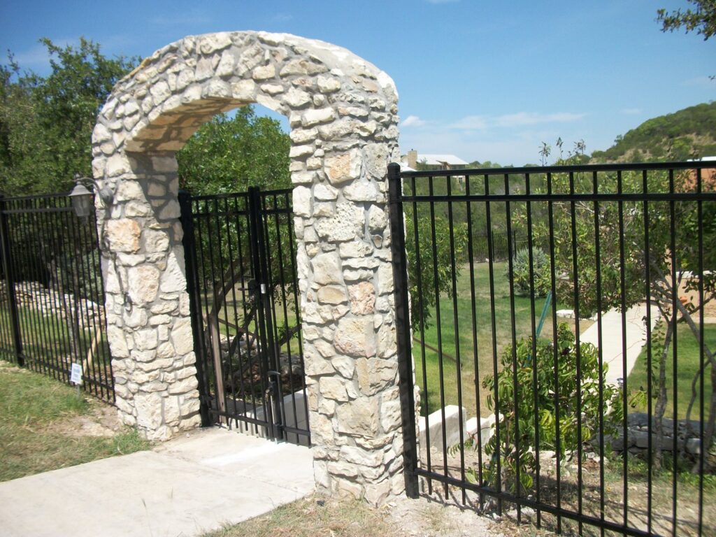 A decorative stone archway with a black metal gate and fence installed by City Fence Co of San Antonio, TX
