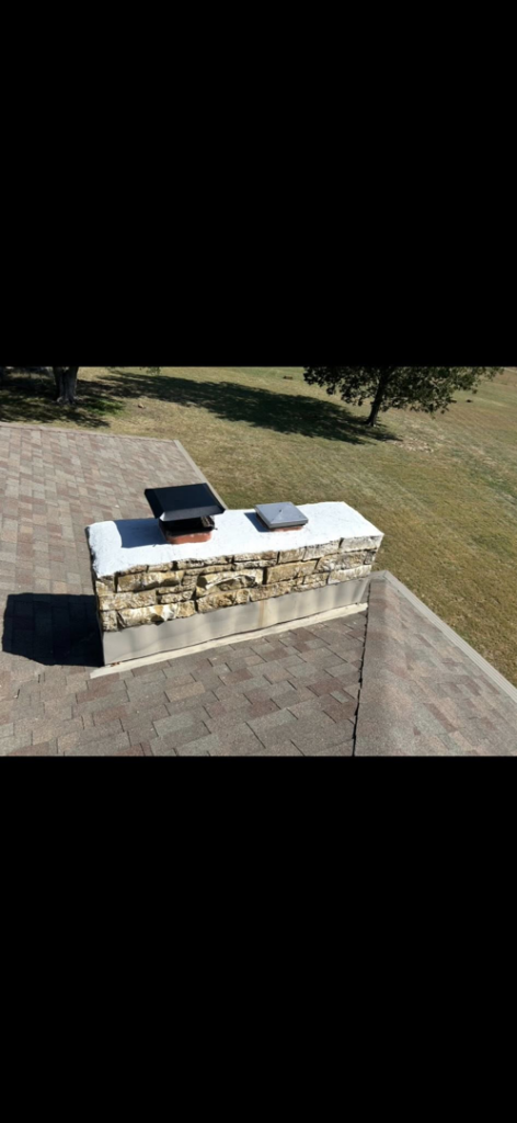 A completed stone veneer chimney installation or repair with two caps on a roof by Harry's Quality Chimney Services in Kansas City, MO