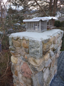 A newly installed chimney cap on a stone chimney, showcasing quality work by Elite Home Solutions in Warwick, RI.