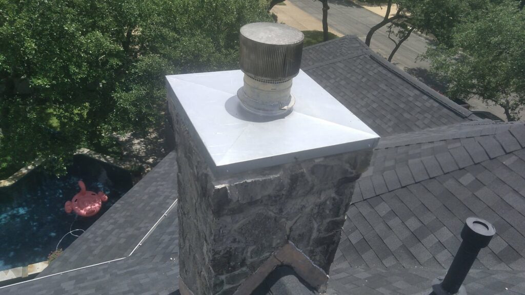 A stone chimney with a new metal cap installed on a roof by The Texan Chimney Sweep San Antonio, TX.