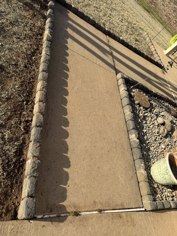 Detailed view of stone edging installed along a concrete pathway, showcasing landscaping services by Perez Lawn Care llc in Oklahoma City, OK.