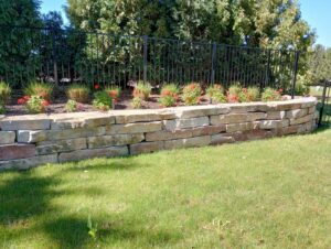A decorative stone retaining wall with a vibrant flower bed next to a lush green lawn by Miguel Landscaping LLC in Janesville, WI.