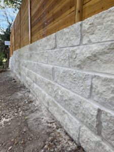 A stone retaining wall with a new wooden fence installed above it by Good Neighbor Fencing and Construction in Austin, TX.