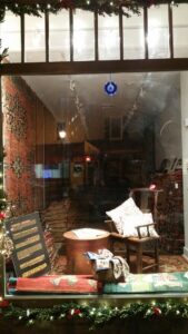 A festive storefront window display showcasing various rugs and home decor items from Woven Legends in Philadelphia, PA.