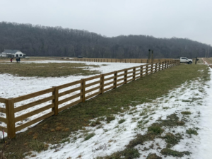 A long, straight wooden farm fence line installed in a snowy field by Richards Fencing in Lynnville, TN