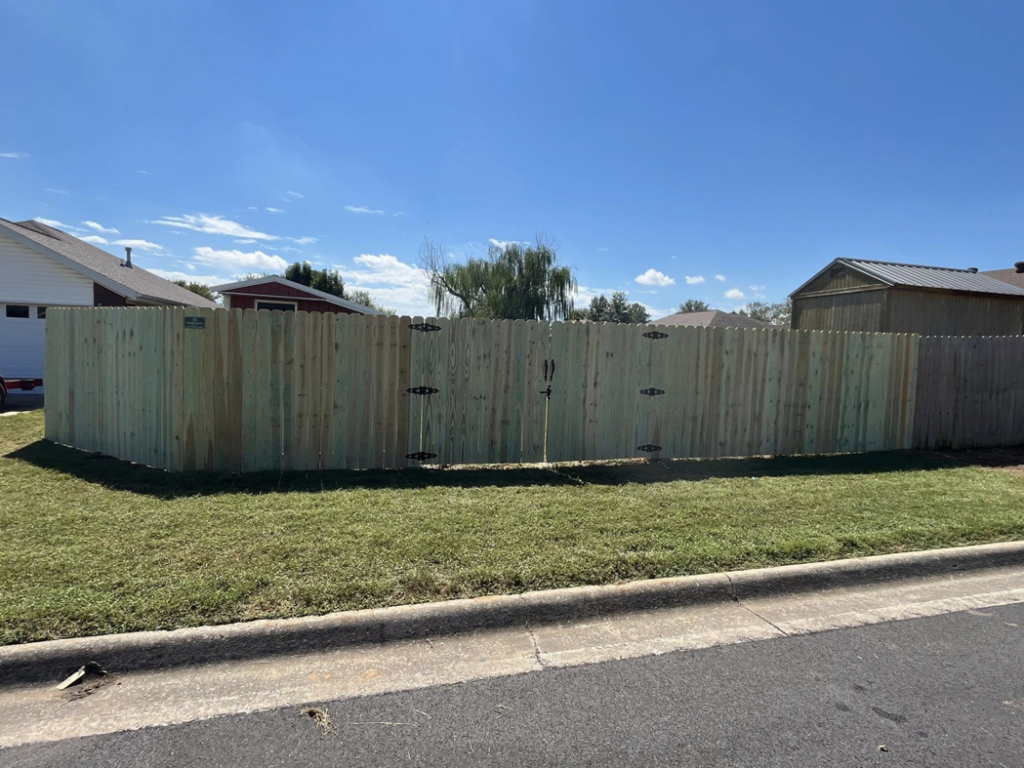 A street view of a green-treated wooden fence featuring two gates, installed by Timber Wolf Fence Co. in Rogers, AR.