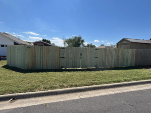 A street view of a green-treated wooden fence featuring two gates, installed by Timber Wolf Fence Co. in Rogers, AR.