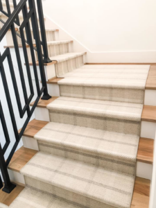 A close-up view of a professionally installed striped carpet runner on a wooden staircase by Southern Star Finishes in Houston, TX.